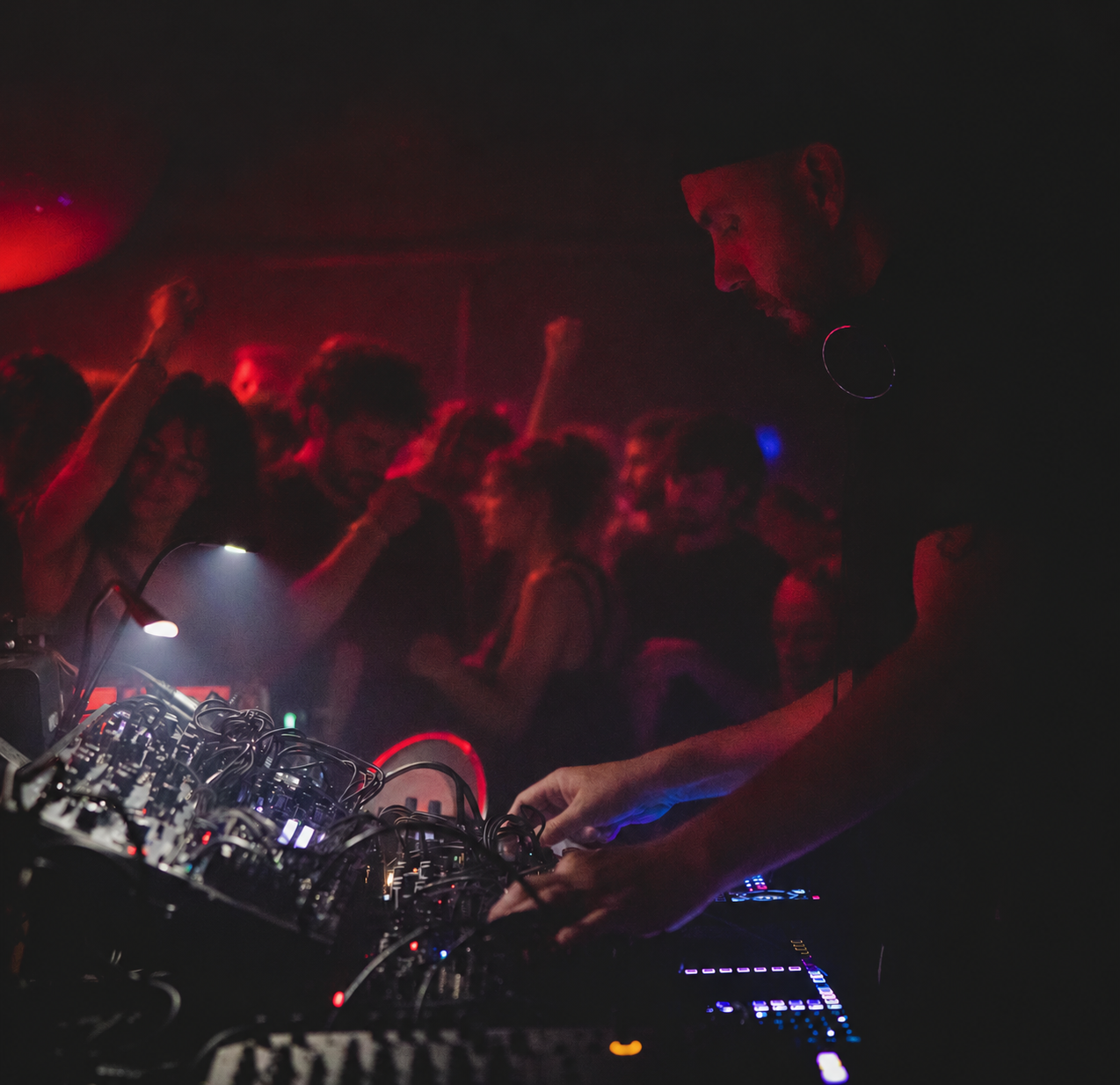 William White at his modular synthesizers with a dancing audience — side view under red club lighting